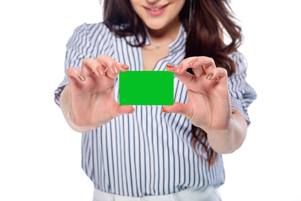 Красивая брюнетка кавказская молодая девушка в белых брюках и полосатой рубашке держа банк или визитная карточка (сохраняется с пути) крупным планом изолированы на белом фоне - Фото, изображение