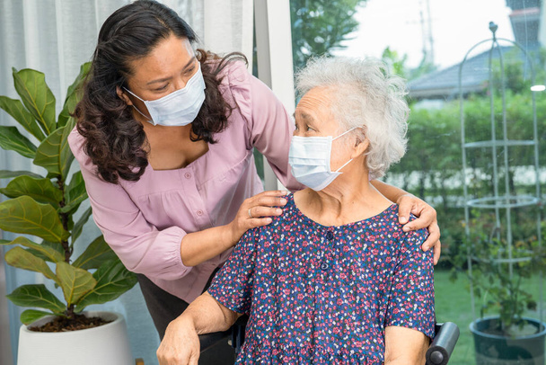 El cuidador ayuda a la anciana asiática mayor o anciana sentada en silla de ruedas y con una máscara facial para proteger la infección por seguridad Covid19 Coronavirus. - Foto, imagen