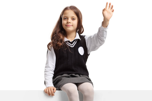 Schoolgirl sitting on a panel and waving isolated on white background - Φωτογραφία, εικόνα