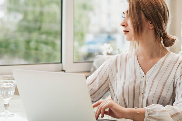 Młoda kobieta biznesu patrząc przez okno podczas pracy na laptopie - Zdjęcie, obraz