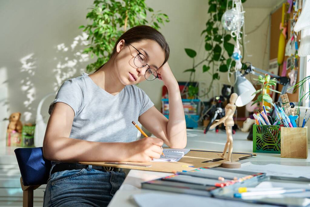 Teenage creative girl artist drawing with a pencil, sitting at the table at home, using awooden mannequin. Creativity, school, hobby, leisure, lifestyle, adolescence, youth concept - Foto, Bild