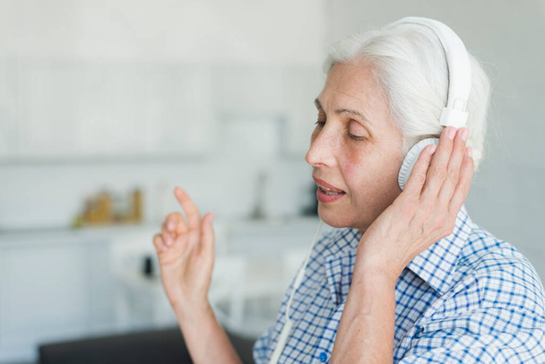 πλευρική άποψη ηλικιωμένη γυναίκα ακούγοντας μουσική ακουστικών τραγούδι. Φωτογραφία υψηλής ανάλυσης - Φωτογραφία, εικόνα