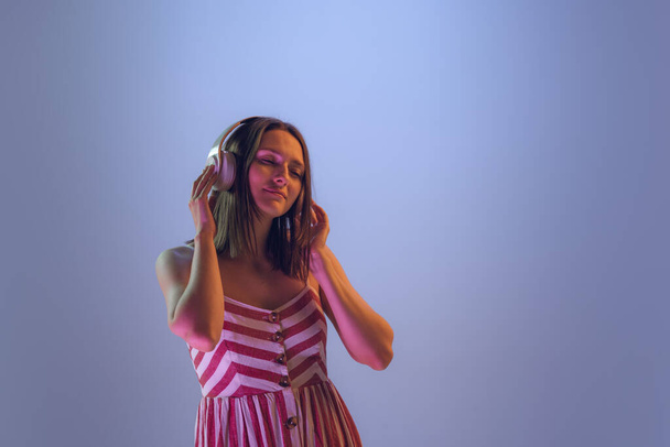Dancing mood. Young beautiful girl in headphones listening to music isolated on blue background in neon. Concept of emotions, facial expression, youth, aspiration, sales - Foto, afbeelding