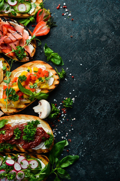 Set of colored sandwiches with tomatoes, prosciutto, vegetables and cheese on a black stone background. Bruschetta. Top view. - Foto, afbeelding