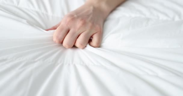 Naisten käsi puristamalla arkki sängyllä, lähikuva, hidastettuna. Käsi tarttuu valkoiseen rypistyneeseen huopaan - Materiaali, video