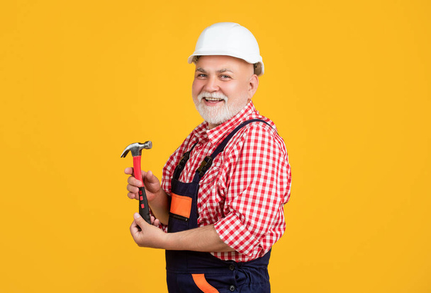 positive senior man carpenter in hard hat on yellow background. - Fotó, kép