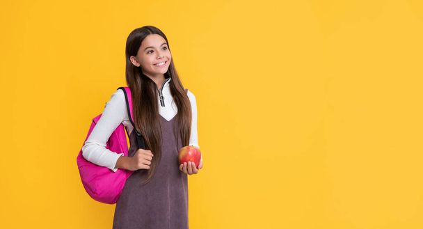 cheerful kid with school backpack and apple on yellow background. - 写真・画像