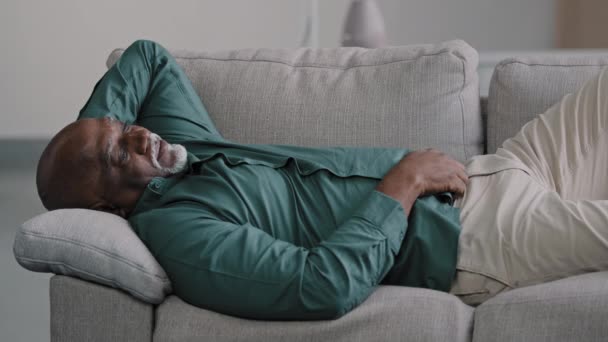 Onnellinen rento afrikkalainen amerikkalainen haaveileva mies levätä sohvalla kotona nauttia rauhallisella tuulella, uninen laiska rauhallinen vanha kypsä liikemies makaa mukava sohva olohuoneessa toimisto stressiä ilmaiseksi rentoutua - Materiaali, video