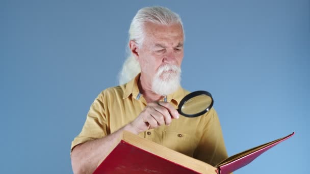 Old man looking at book with magnifying glass - Imágenes, Vídeo
