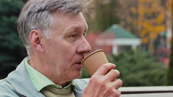 Portrait dreaming caucasian senior man retired grandpa relaxing in autumn park feel calmness harmony adult male 70s aged pensioner drink hot tea disposable cup rest weekend smiling turn head at camera - Footage, Video