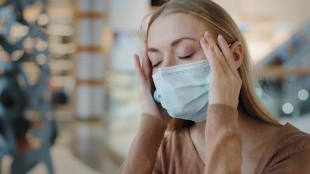 Innenporträt kaukasische Frau in medizinischer Maske, die sich unwohl fühlt, Kopfschmerzen, die Schläfen massiert, die Symptome der Coronavirus-Pandemie aufweist, kranke Frau aus nächster Nähe, die an Migräne-Grippe leidet - Filmmaterial, Video