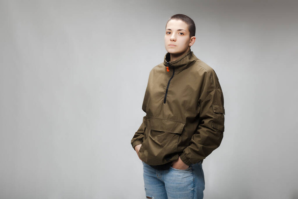 Girl with short hair wearing jacket and jeans against gray background. - Zdjęcie, obraz