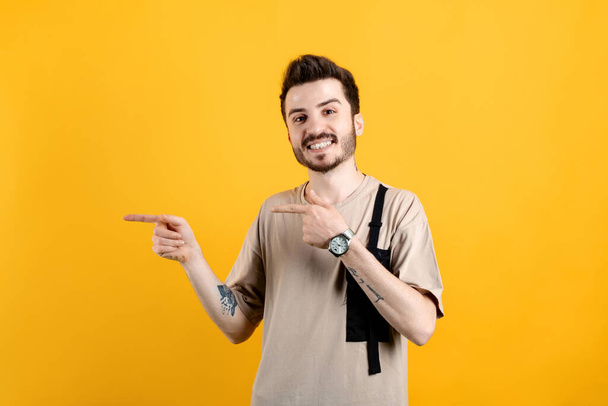 Homme caucasien joyeux portant des vêtements décontractés posant isolé sur fond jaune souriant et regardant la caméra pointant avec deux mains et doigts sur le côté gauche. - Photo, image