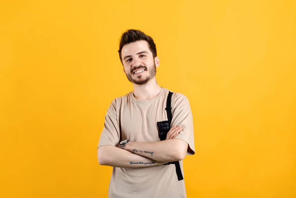 Homme caucasien portant t-shirt beige posant isolé sur fond jaune souriant avec les bras croisés regardant la caméra. Personne positive. - Photo, image