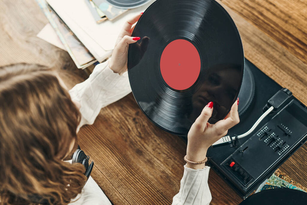 Young woman listening to music from vinyl record player. Playing music on turntable player. Female enjoying music from old record collection at home. Stack of analog vinyl records. Retro and vintage music style. Music Passion and hobby - Фото, зображення