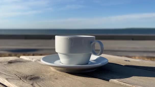 taza de café en la mesa de madera en la playa café mar en el horizonte olas de agua y el cielo azul - Metraje, vídeo