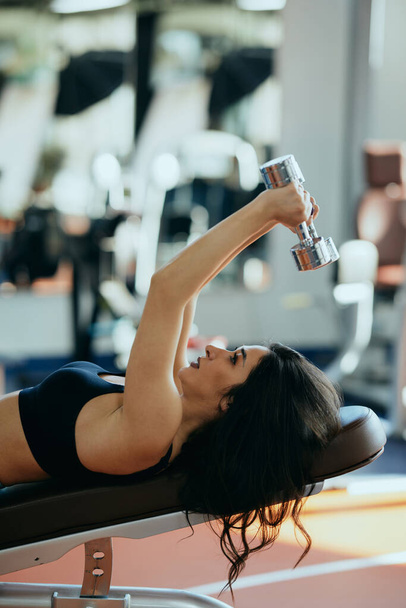 Ein kräftiger Bodybuilder lehnt sich in einem Fitnessstudio auf eine Bank und macht mit Kurzhanteln Workouts für die Brust. - Foto, Bild