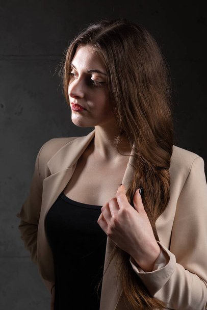 Portrét mladé brunetky s dlouhými vlasy ve studiu. Dramatická fotografie v tmavých barvách. - Fotografie, Obrázek