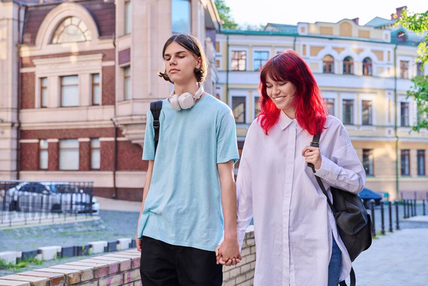 Couple of happy teenage friends walking holding hands, outdoor, on city street. Friendship, romantic, youth, leisure, relationship, lifestyle concept - Foto, imagen