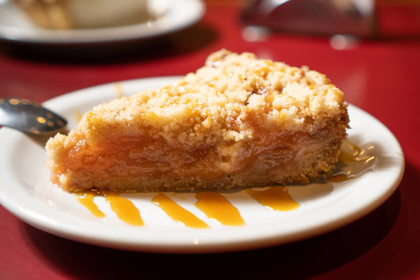 close-up de uma porção individual de torta de maçã com molho de caramelo doce. está em uma placa branca em uma mesa vermelha. - Foto, Imagem