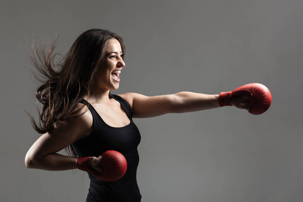 beautiful girl exercising karate punch and screaming against gray background - Foto, imagen