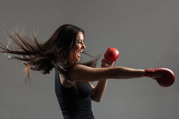 beautiful girl exercising karate punch and screaming against gray background - Foto, Imagem