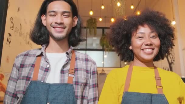 Twee jonge startup barista partners met schorten staan bij casual cafe deur, armen gekruist, kijken naar de camera met en gastvrije glimlach, gelukkig en vrolijk met coffeeshop service banen, MKB-ondernemers. - Video