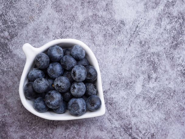 Top view, fresh blueberries in leaves-shaped white plate on dark grey background. Flat lay with copy space. Concept for healthy eating and nutrition, Superfood - Foto, afbeelding