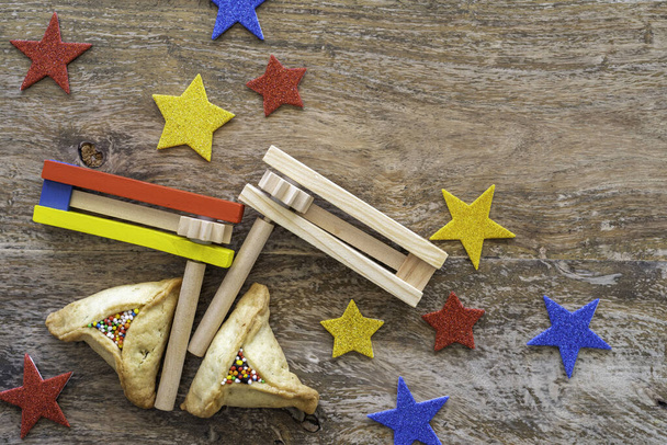 Διακοσμητικά noisemakers, παραδοσιακά μπισκότα Hamantaschen, πολύχρωμα αστέρια για εβραϊκές διακοπές Purim σε ξύλινο φόντο.   - Φωτογραφία, εικόνα