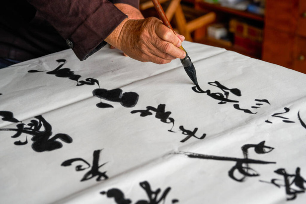 An old calligrapher is writing and creating calligraphy works. Translation: It rains on the pond with light thunder outside Liuwai, and the sound of rain drops and smashes the lotus. - Fotografie, Obrázek