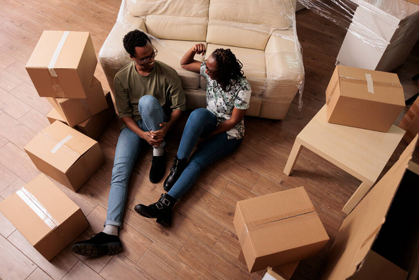 Afrikkalainen amerikkalainen pariskunta nauttimassa uudesta omaisuudesta, tauolla lattialla muutettuaan yhteen. Rentoutuminen muuttopäivänä, ensimmäisen asunnon ostaminen asuntolainalla. Ylhäältä. - Valokuva, kuva