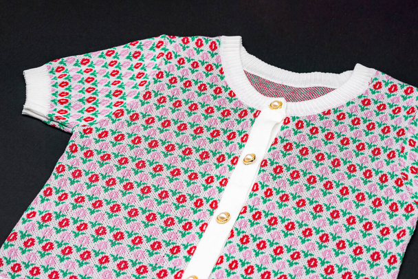 plano blanco punto rosa rojo flor patrón suéter forma de camiseta con botones de perla y círculo de oro sobre fondo negro con luz de estudio - Foto, Imagen