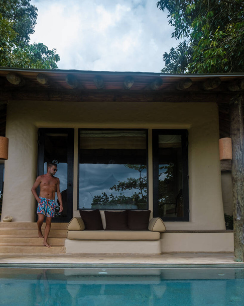 European man at infinity pool in Thailand looking out over the ocean, luxury vacation in Thailand, private pool villa. High quality photo - Foto, afbeelding