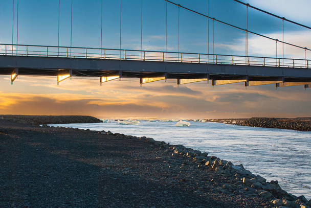 A mesmerizing shot of a hanging bridge over a coastline in the sunset. - Foto, Bild