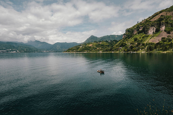 A beautiful shot of a fisherman in a boat in Lake Atitlan with mountains in the background on a cloudy day. - Foto, Imagem
