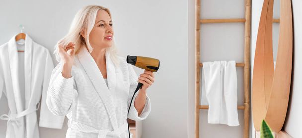 Morning of mature woman with hair dryer in bathroom - Foto, imagen