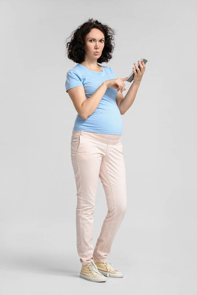 Upset young pregnant woman using calculator on light background - Foto, Bild