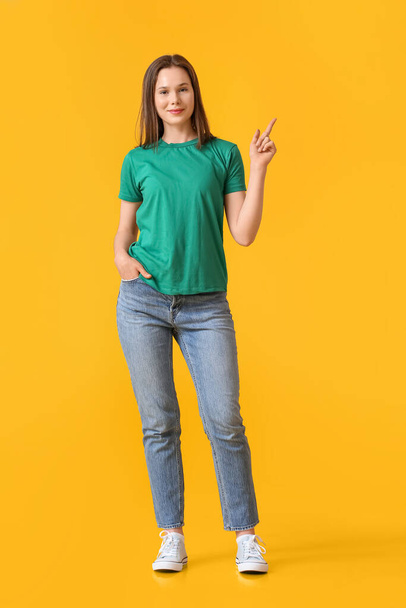 Hübsche junge Frau im grünen T-Shirt zeigt auf etwas auf gelbem Hintergrund - Foto, Bild