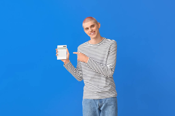 Mladý muž ukazuje na kalkulačku na modrém pozadí - Fotografie, Obrázek