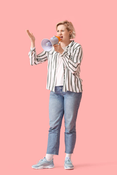 Beautiful blonde woman shouting into megaphone on pink background - 写真・画像