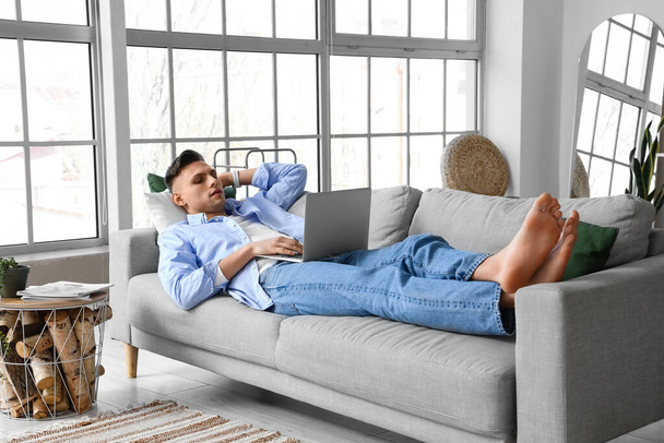 Jeune homme pieds nus utilisant un ordinateur portable sur le canapé à la maison - Photo, image