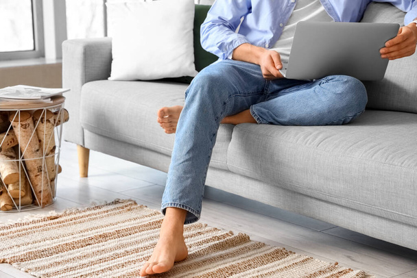 Young barefoot man using laptop on sofa at home - Fotoğraf, Görsel