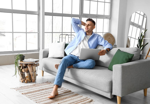 Nuori paljain jaloin mies sylimikro istuu sohvalla kotona - Valokuva, kuva