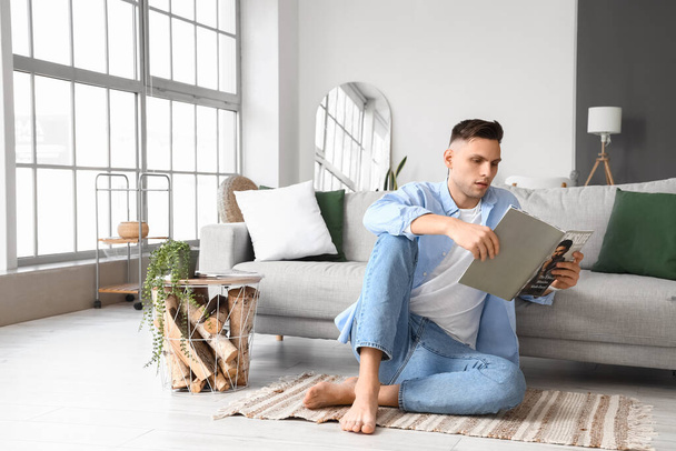 Joven hombre descalzo leyendo revista en casa - Foto, Imagen
