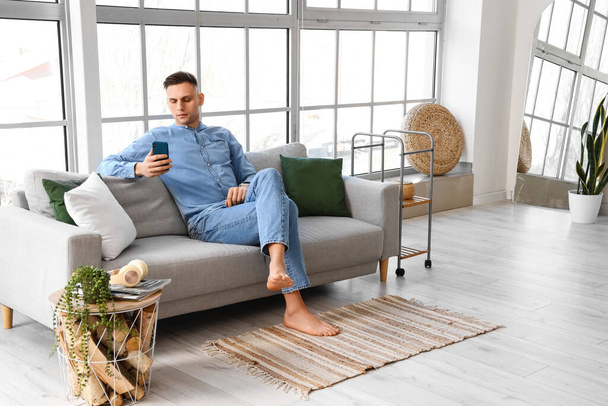 Young barefoot man using mobile phone on sofa at home - Foto, Bild