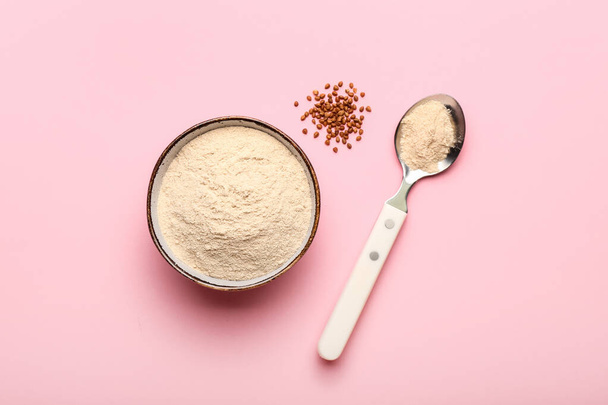 Bowl of flour, spoon and buckwheat grains on pink background - Foto, Imagen