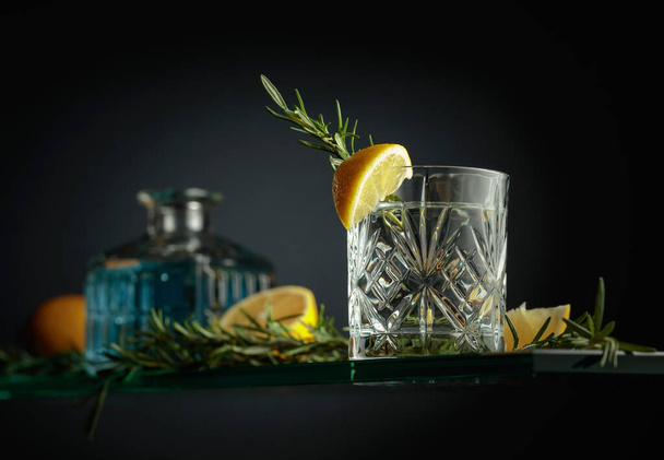 Kaltes Erfrischungsgetränk mit Zitrone und Rosmarin. Gin Tonic Cocktail im Kristallglas. - Foto, Bild