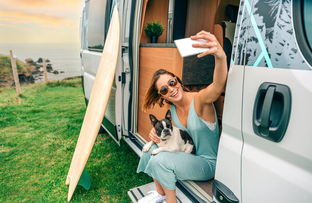 Jeune femme prenant des photos assis avec son chien terrier boston à la porte du camping-car - Photo, image