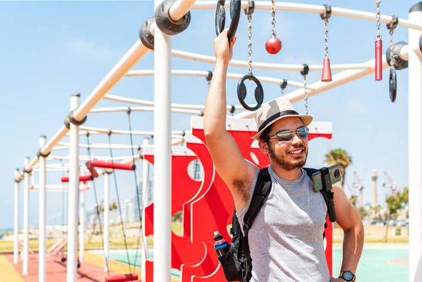 Un jeune touriste masculin du Moyen-Orient avec un sac à dos dans l'aire de jeux extérieure profitant de l'été - Photo, image