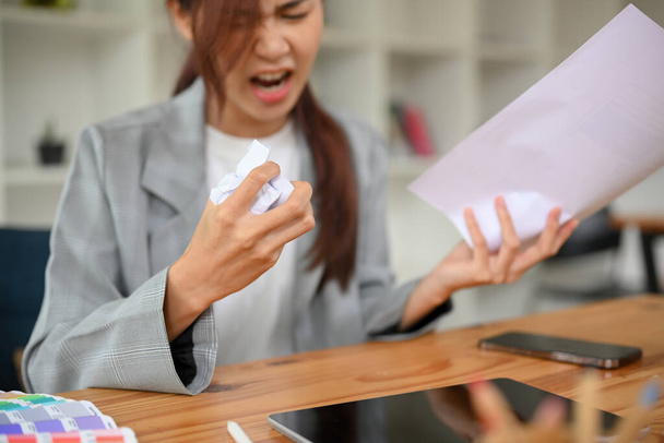 Loca mujer de negocios asiática enojada o jefa arrugando un documento, gritando en la oficina, insatisfecha con su proyecto de trabajo. Imagen recortada, Papel arrugado en mano de mujer. - Foto, Imagen